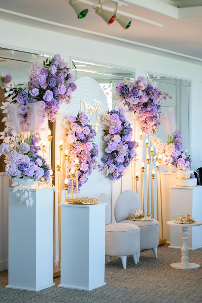Luxurious wedding decor with purple floral arrangements and upholstered chairs.